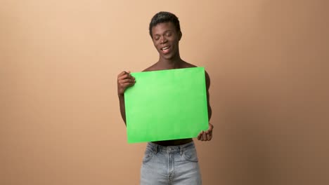 happy young black shirtless man with a green chroma banner looking at camera with beige background