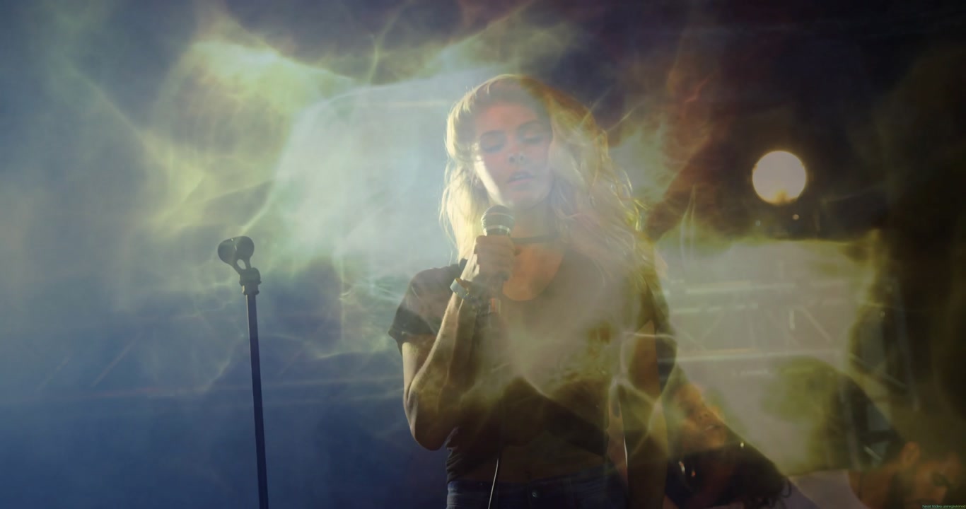 Female singer gripping mic, tossing head back, meeting gaze, creating music vibe under lights