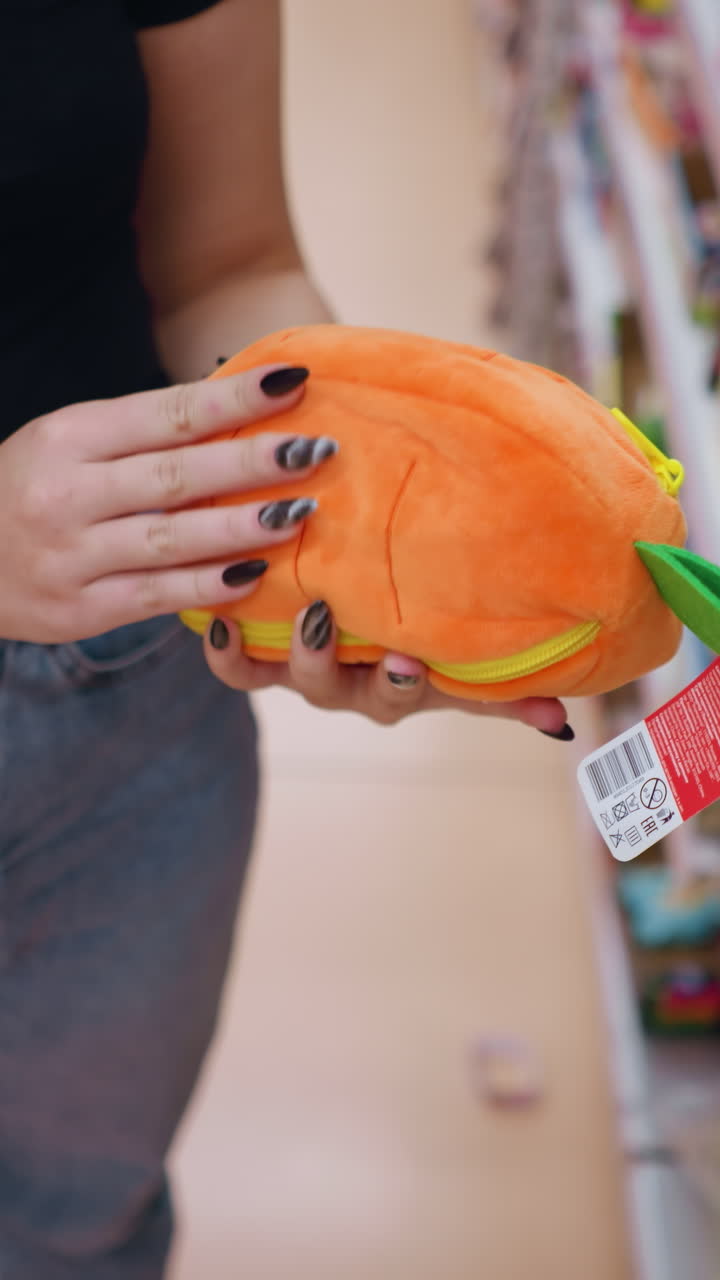 primer plano de arriba hacia abajo de una mujer recogiendo un bolso naranja y verde vibrante de la estantería de la tienda mientras observa los detalles, el comprador navega por accesorios elegantes en un entorno minorista