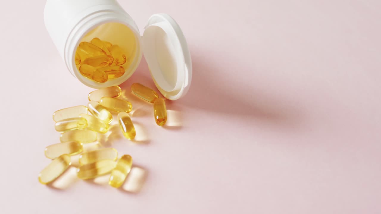 video de una caja de pastillas blanca derramando cápsulas de aceite sobre un fondo rosa con espacio para copiar