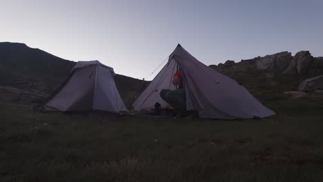 early morning sunrise tent opening from the inside and young hiker getting out with red down jacket