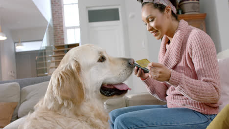 happy biracial woman with golden retriever dog using smartphone and credit card at home, slow motion