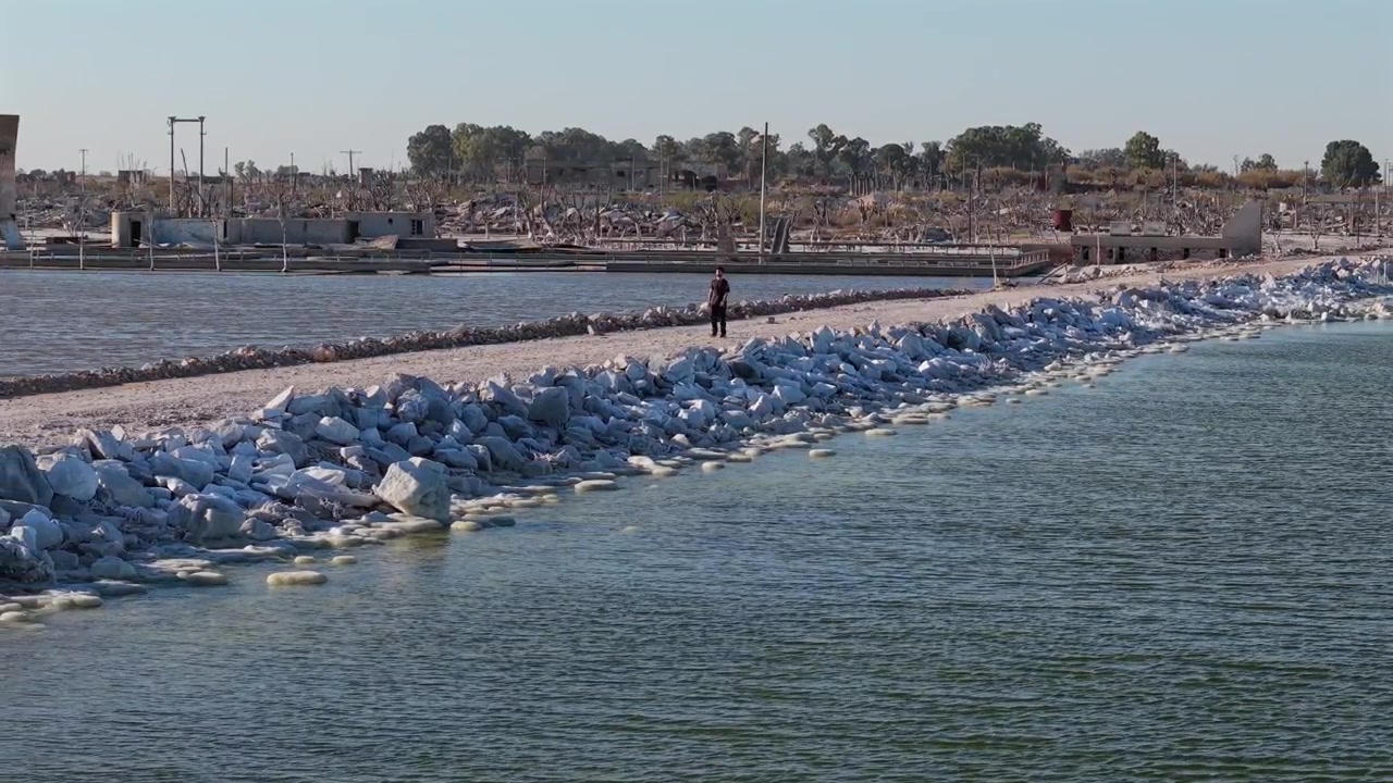Adolfo Alsina, Buenos Aires Eyaleti, Arjantin'deki Epecuen Gölü kıyısında, 1985'teki yıkıcı selin yaşandığı Villa Epecuen'in tuzla kaplı harabelerinin yanında yürüyen adam, drone ile çekilen eğik geri çekme takip görüntüsü