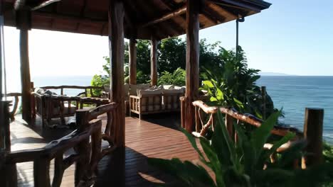 relax on a beautifully designed deck surrounded by vibrant greenery and enjoy panoramic views of the ocean and coastline under a clear sky.