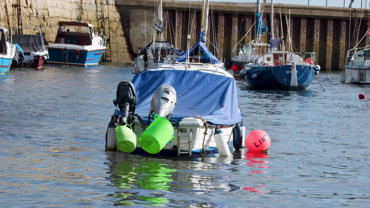 A small motorboat with green buoys drifts calmly in Dysart harbor, bright daylight, steady shot