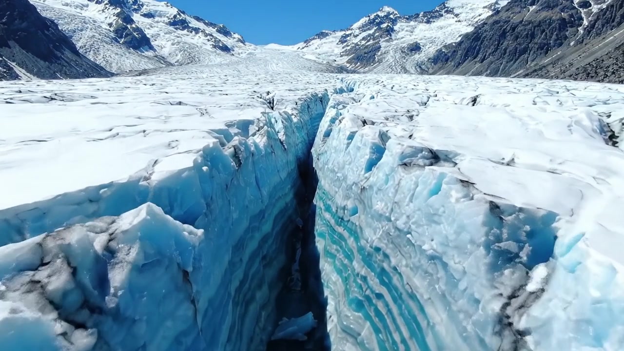 Vista aerea mozzafiato di un vasto ghiacciaio profondamente crepato da forze naturali, mostrando maestose formazioni di ghiaccio sotto cieli azzurri e limpidi.