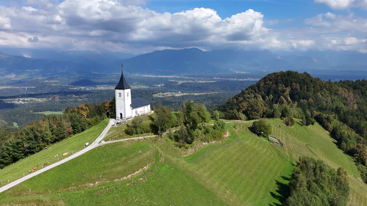 Aerial orbit view of Catholic Church of Saint Primus and Felician sitting atop a hill overlooking Jamnik Slovenia