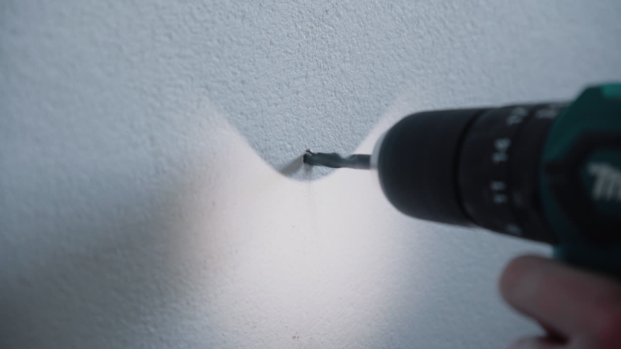 집에서 흰색 시멘트 콘크리트 벽에 구멍을 뚫기 위해 무선 전동 드릴을 사용하는 젊은 남성 잡역부