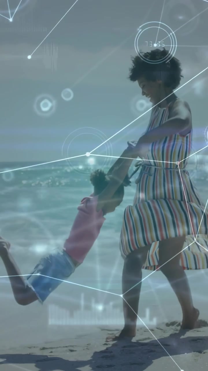 Vertical video: Woman holding child's hands, swinging her on shoreline for play, tech HUD overlaid