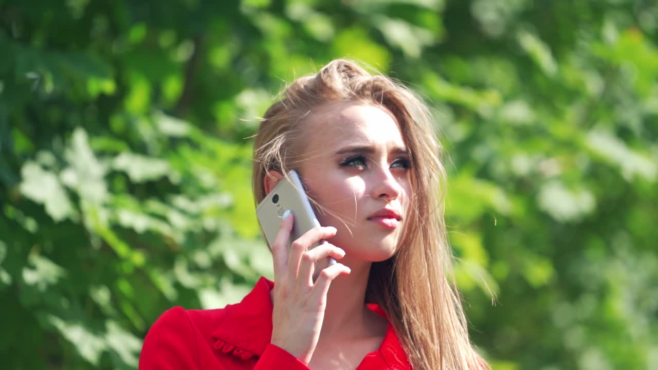 Sad woman's face outdoors. Beautiful young female talking on the mobile phone. Portrait of a pretty lady with a phone. Close-up. Slow motion.