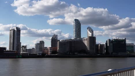 Panning-shot-London-skyline-by-the-Thames-river,-Waterfront-modern-skyscrapers,-Blue-sky-with-clouds