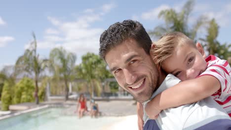 retrato de un padre caucásico feliz llevando a su hijo a la piscina en la casa de la playa
