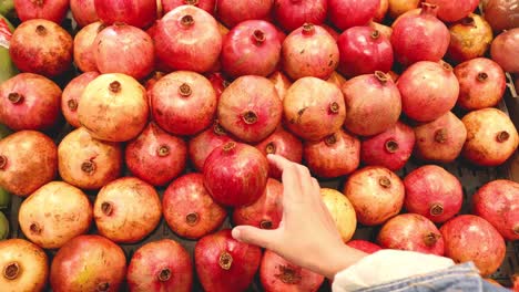 hand picking pomegranate from a fruit display