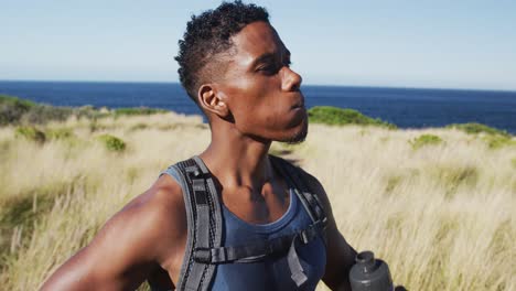 African-american-man-exercising-outdoors-drinking-water-in-countryside-on-a-coast