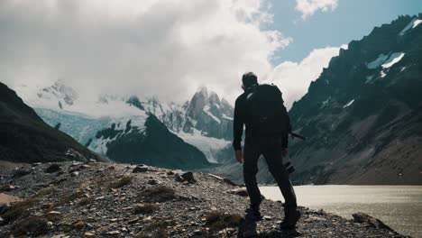 Hiker-With-Camera-And-Backpack-Walking-Along-The-Laguna-Torre-With-Cerro-Torre-And-Glacier-In-The-Background-In-El-Chalten,-Argentina