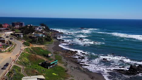 Aerial-drone-with-a-view-of-the-beach-and-people-and-children-playing-with-a-general-view-of-the-houses-on-the-beach-location-is-infiernillo-beach-in-pichilemu-chile-colchagua-cardenal-caro