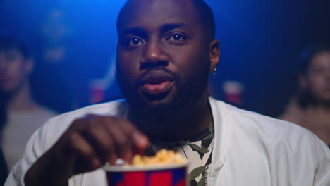 african man eating popcorn in movie theater.