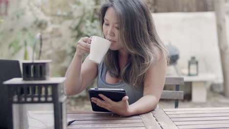 focused woman sitting at table in outdoor cafe with tablet