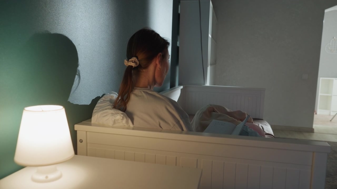 Caucasian mother soothing infant at night, tender nursery moment with bedside lamp glow, female parent holding newborn on crib edge, gentle rocking, warm soft atmosphere and quiet lullaby mood