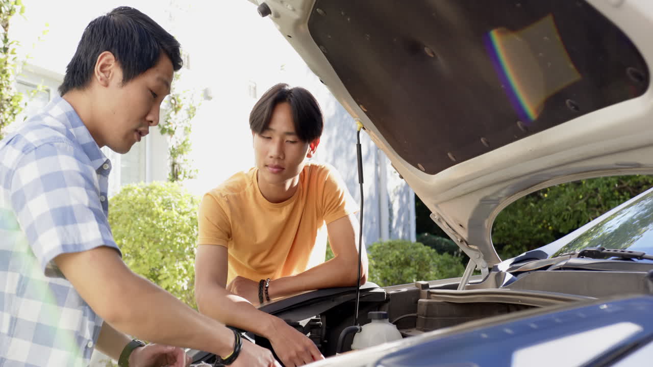 Examining car engine, asian father teaching son about vehicle maintenance outdoors