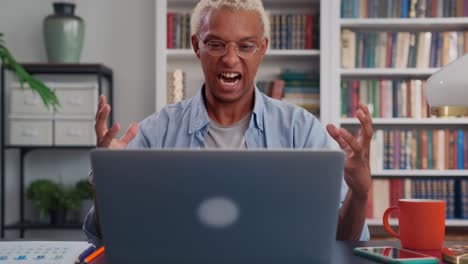 young embittered african american man sits at table with laptop in office