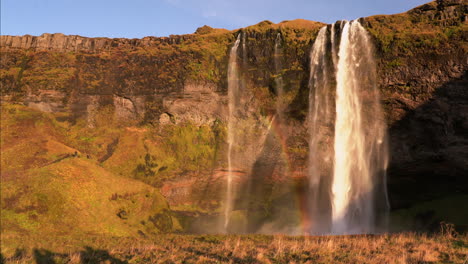 static wide shot of icelandic seljalandsfoss waterfall with rainbow reflection during sunset light in iceland