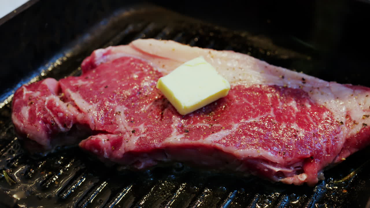 Bistecca di manzo che cuoce su una piastra grill guarnita con rosmarino fresco e condimenti