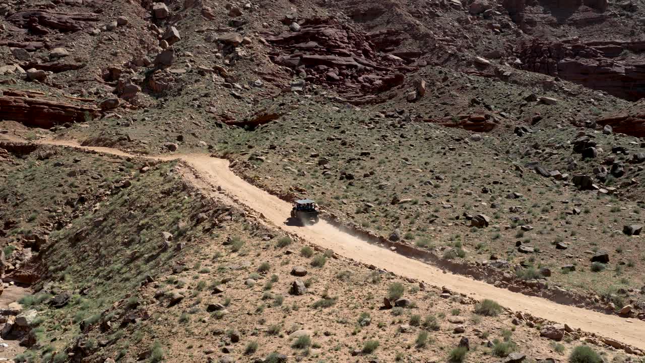 off road adventure with Utility terrain vehicle moves along dusty dirt trail cutting through arid terrain with desert biome along Chicken Corners trail near Moab in Grand County Utah, zoom out reveal