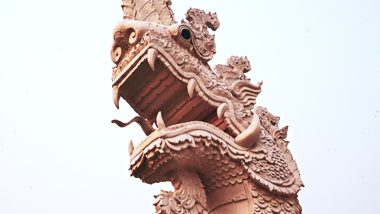 Testa di una statua di drago in pietra ornata che ruggisce con fauci aperte e zanne.