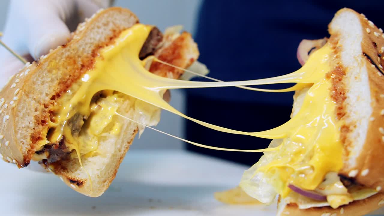 Tasty hot cheeseburger. Juicy burger in chef's hands with melted cheese. Ready hamburger with appetizing filling. Close-up. Fast food