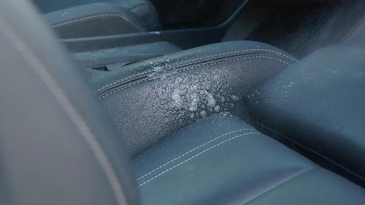 Spraying cleaning product on to white mark on black car leather seat bolster with white paint