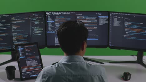 back view of asian man developer working with tablet while write code with multiple computer screens in green screen studio