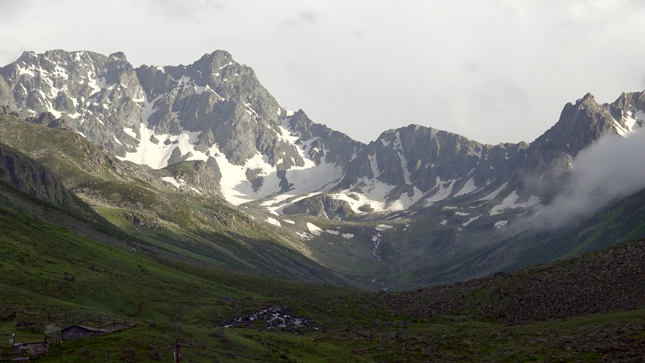 Nuvole che si muovono sopra cime montuose innevate in una valle verde