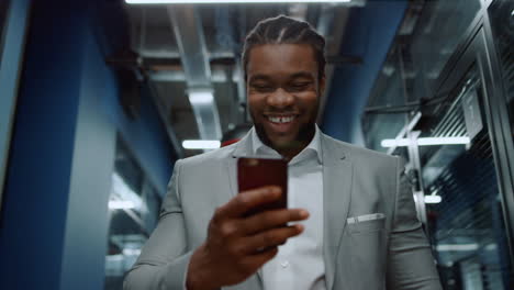 African-businessman-reading-message-in-corridor.-Afro-guy-getting-good-news