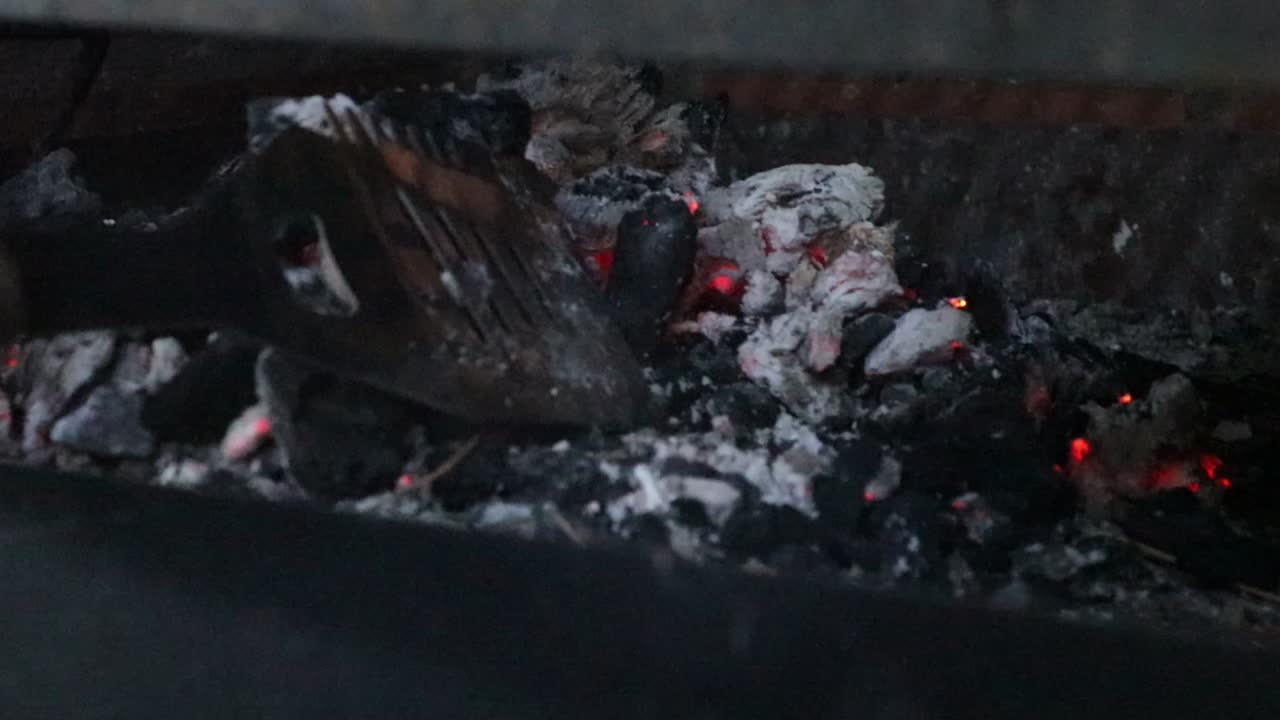 Men's hand holds a metal spatula, trying to revive the fire, and break the coal while still warm, small carbon particles, ashes and sparks.