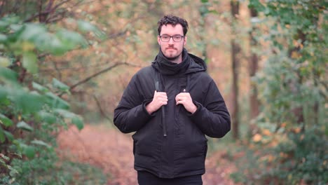 un hombre europeo de barba alegre con gafas de moda se encuentra en medio de los tonos de un bosque de otoño mixto, irradiando felicidad y calidez al ver a los espectadores, emanando vibraciones positivas puras