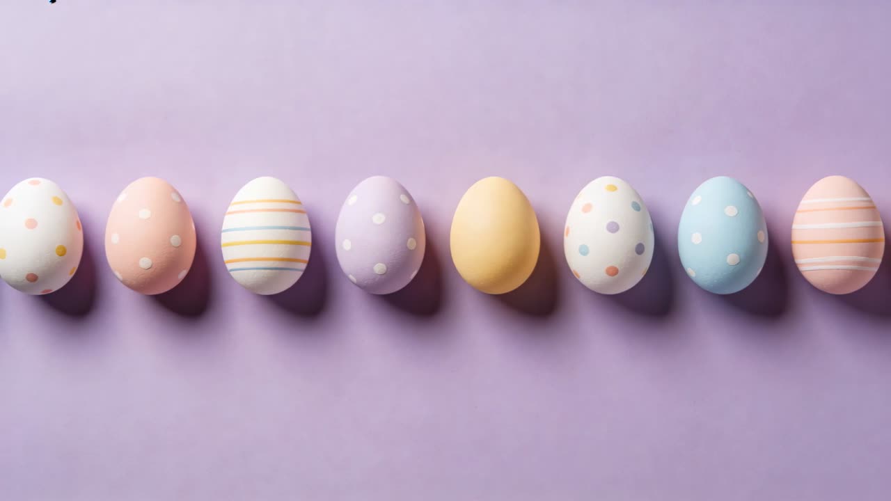 Panning camera bringing row of painted pastel eggs across lavender backdrop, showing patterns