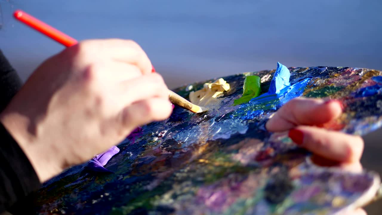 summer,outdoors, close-up of female hands of the artist and a palette with paints, the artist mixes paints with a brush on the palette