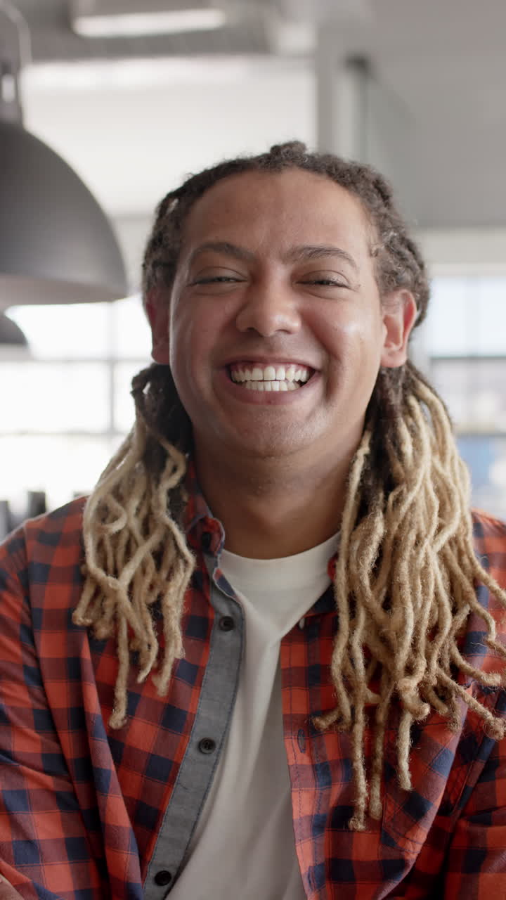 Vertical video of portrait of happy biracial businessman smiling in office