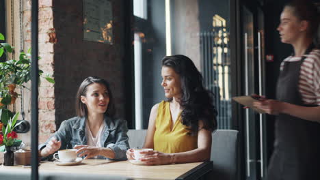 women having coffee and chatting with a waitress in a cafe