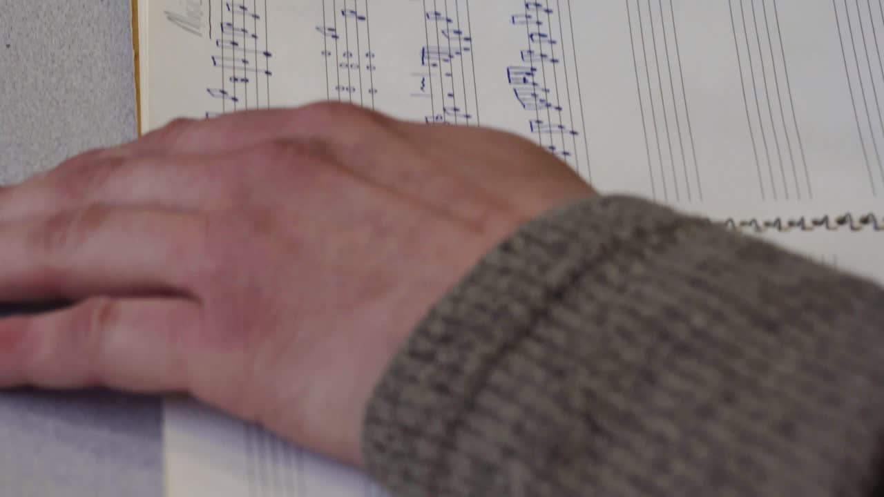 un hombre escribiendo música en un bloc de notas sobre una mesa blanca - cerrar la bandeja