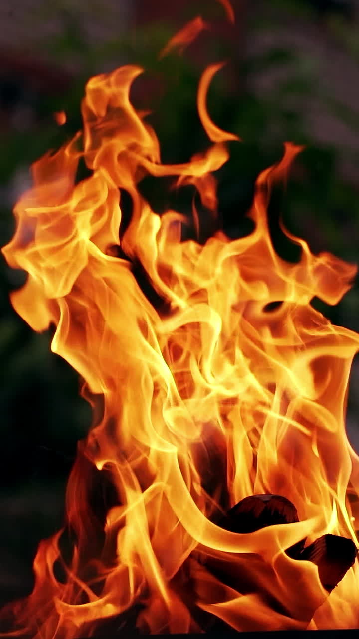 Smoldered logs burned in vivid fire on the house background. Fantastic orange and yellow flame of campfire outdoors. Close-up. Vertical video