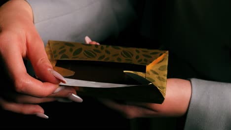 top view of a woman's hand unwrapping and revealing a chocolate bar with golden packaging on black background