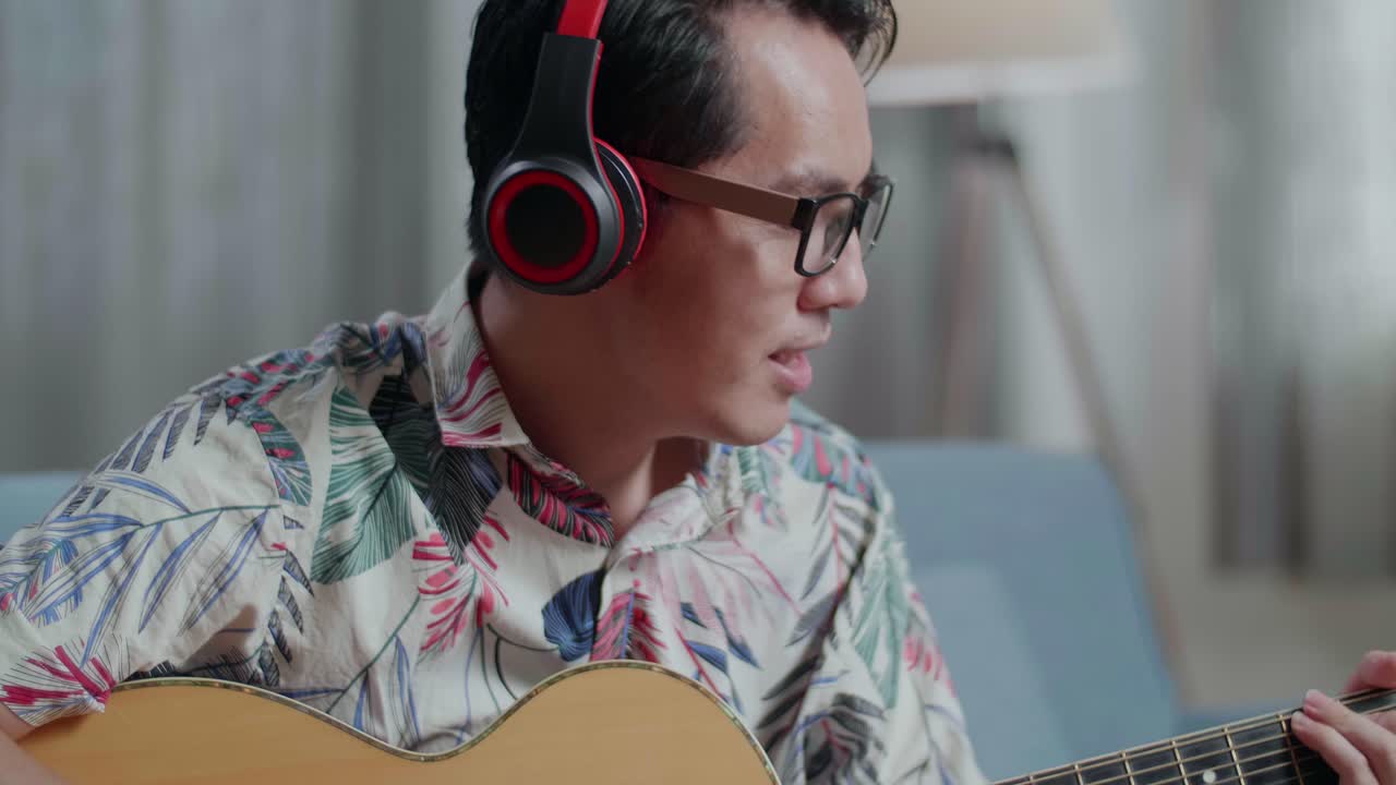 집에서 노래하고 기타를 연주하는 헤드폰을 착용한 테이블 위에 노트북을 가진 아시아인 작곡가의 클로즈업