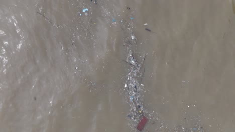 baja altitud de arriba hacia abajo toma de drone de agua contaminada llena de basura flotante y escorrentía de río fangosa mezclándose con agua tropical turquesa de bali indonesia