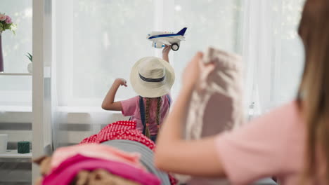 Daughter-plays-with-plane-woman-folds-belongings-on-sofa