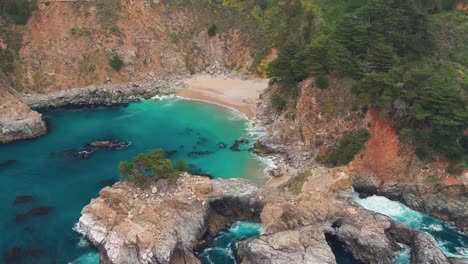 La-Cala-En-El-Parque-Estatal-Julia-Pfeiffer-Burns,-California,-Con-Una-Revelación-Aérea-De-Paralaje-De-Las-Cataratas-Mcway.