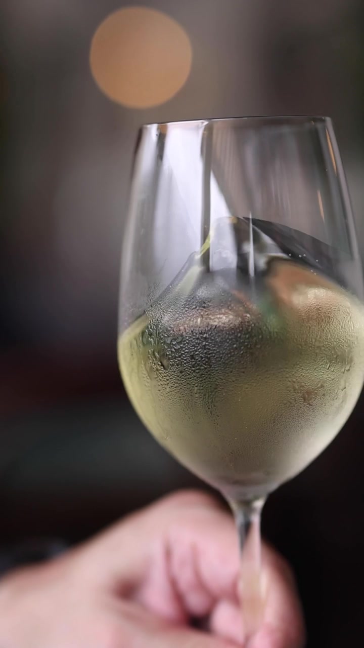 Una mano regge un bicchiere di vino bianco coperto di condensa, facendo roteare delicatamente il liquido all'interno.
