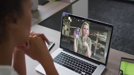 african american businesswoman sitting at desk using laptop having video call with female colleague