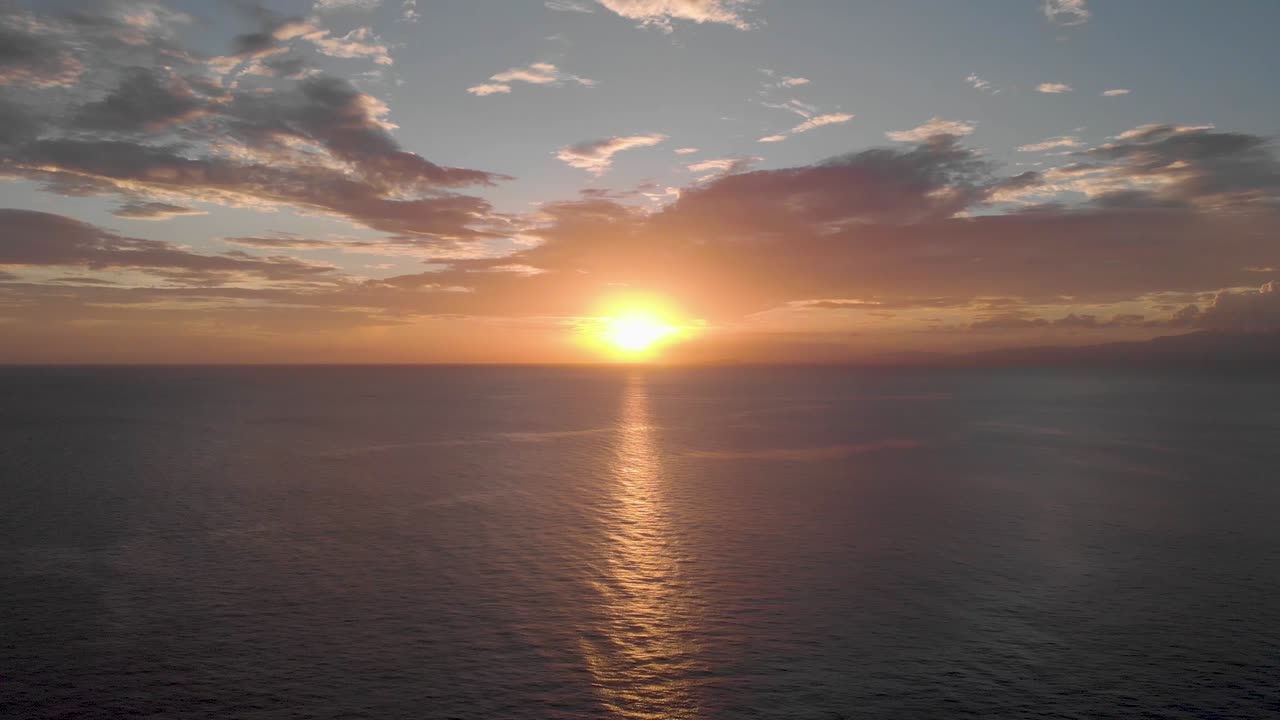 Aerial Cinematic shot of vibrant beautiful sunset over huge cliffs in Uluwatu Bali with deep blue crashing waves at the base of the ocean
